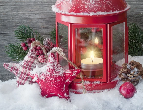rote Laterne mit brennender Kerze, Sternen und Tannenzweigen im Schnee